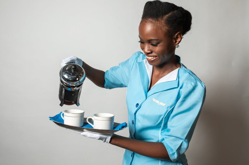 pexels-photo-5778260 A cheerful flight attendant in a blue uniform pouring coffee with a French press.